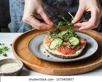 Healthy Toast  With Cream Cheese, Salmon, Fresh Cucumber, Capers, Red Onion, Black Pepper And And An Uncertain Woman Lays On A Sandwich Pea Sprouts . 
