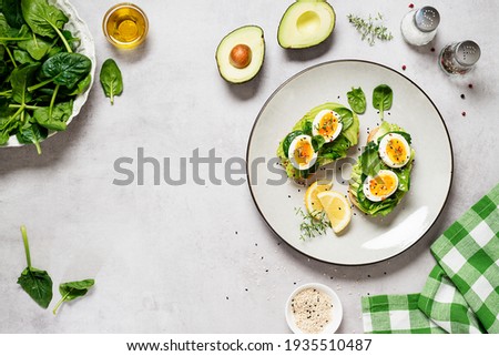 Healthy toast with sliced avocado, boiled eggs, spices and fresh spinach. Delicious breakfast or snack on gray stone background. top view, space for text