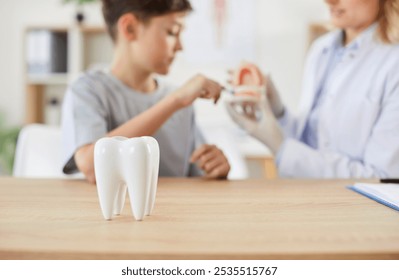 Healthy tooth model on wooden table, close-up. Dentist with jaw model teaching boy how to brush teeth, blurry. Concept tooth dentist child, dental fillings, health care and medicine - Powered by Shutterstock