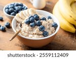 Healthy vegan dairy free oatmeal porridge with fresh blueberries and banana slices in bowl on wooden table background, closeup view