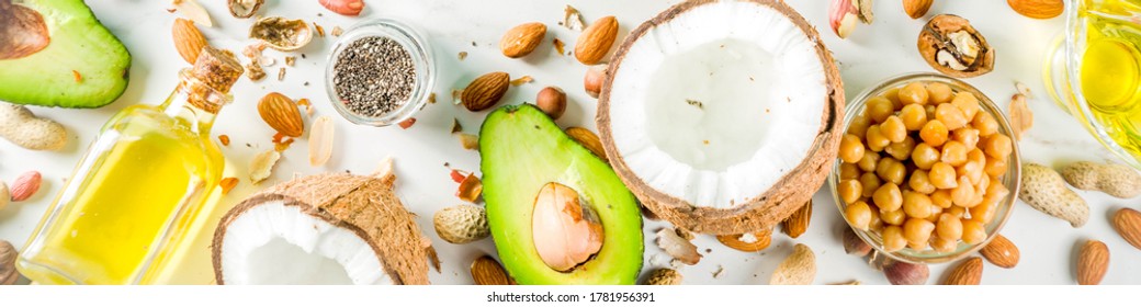 Healthy vegan fat food sources, omega3, omega6 ingredients - almond, pecan, hazelnuts, walnuts, olive oil, chia seeds, avocado, coconut, dark green background copy space banner