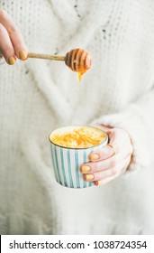 Healthy vegan turmeric latte or golden milk with honey in hands of woman wearing white sweater