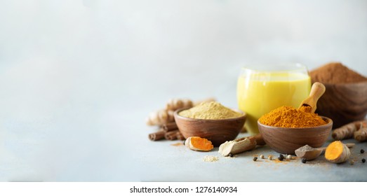 Healthy vegan turmeric latte or golden milk, turmeric root, ginger powder, black pepper over grey concrete background. Spices for ayurvedic treatment. Alternative medicine concept.