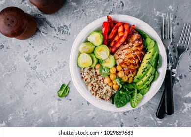 Healthy vegetable buddha bowl lunch with grilled chicken and quinoa, spinach, avocado, brussels sprouts, red paprika and chickpea on gray background. Top view.