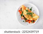 Healthy vegetable loaded omelette. Top view on a plate over a white marble background.