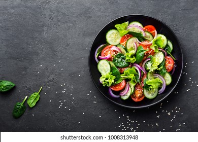 Здоровый овощной салат из свежих помидоров, огурцов, лука, шпината, салата и кунжута на тарелке. Диета меню. Вид сверху.
