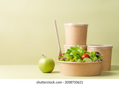 Healthy vegetable salad in recyclable cardboard container. Food delivery, healthy food menu for home or office concept. Green background, side view