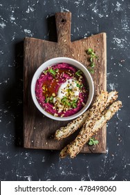 Healthy vegetarian beet hummus and puff pastry bread sticks on a wooden rustic board on a dark background