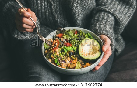 Healthy vegetarian dinner. Woman in jeans and warm sweater holding bowl with fresh salad, avocado, grains, beans, roasted vegetables, close-up. Superfood, clean eating, vegan, dieting food concept