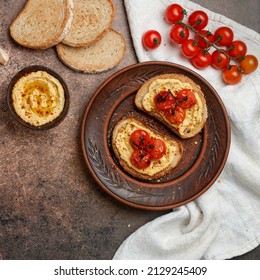 Healthy vegetarian sandwiches with whole grain bread, hummus, baked tomatoes and spices. bruschetta. A delicious snack for gourmets. Rustic style. Selective focus, top view, square picture