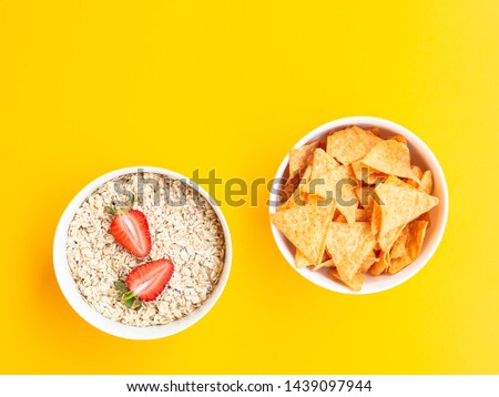 Healthy vs unhealthy food and dieting concept. Fried chips or nachos and oat flakes with strawberries in bowls isolated on yellow color studio background with copy space. Flat lay, view from top.