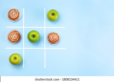Healthy vs unhealthy food, green apples vs cinnamon buns in tic tac toe or noughts and crosses game, horizontal, top view,  copy space