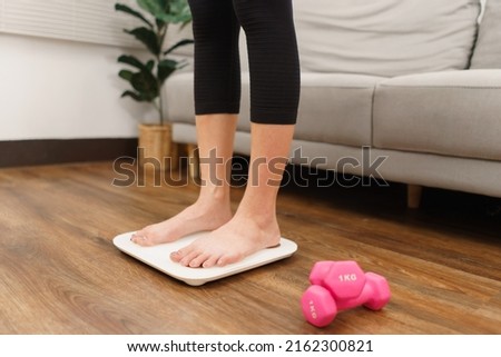 Healthy and weight loss concept, Young Asian woman stand on weighing scales to checking her weight.