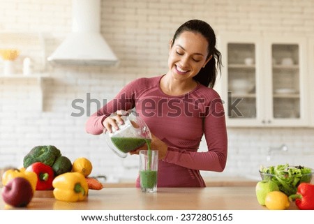Healthy Weight Loss Nutrition. Glad Fit Lady Pouring Green Detox Smoothie In Glass, Cooking Organic Meal For Slimming, Enjoying Diet Routine At Modern Kitchen Indoors, Wearing Sportswear
