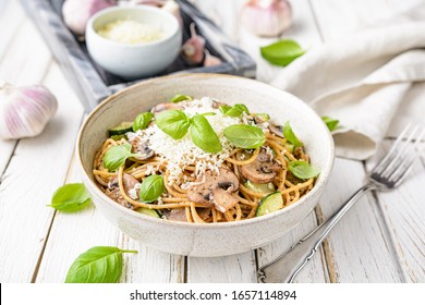 Healthy whole wheat spaghetti with sauteed mushrooms garlic and zucchini, topped with grated cheese and basil leaves on rustic wooden background - Powered by Shutterstock