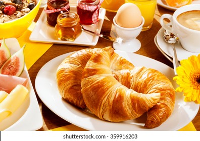 Healthy wholesome breakfast with two fresh croissants on a plate with a boiled egg, fresh fruit and cheese, cereal and a cup of coffee, focus to the croissants