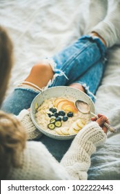 Healthy Winter Breakfast In Bed. Woman In Woolen Sweater And Shabby Jeans Eating Vegan Almond Milk Oatmeal Porridge With Berries, Fruit And Almonds. Clean Eating, Vegetarian Food Concept