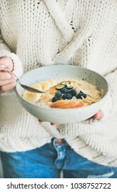 Healthy Winter Breakfast In Bed. Woman In Woolen Sweater And Jeans Eating Vegan Almond Milk Oatmeal Porridge With Berries, Fruit And Almond. Clean Eating, Vegetarian Food Concept