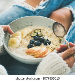 Healthy Winter Breakfast In Bed. Woman In Woolen Sweater And Shabby Jeans Eating Vegan Almond Milk Oatmeal Porridge In Bowl With Berries, Fruit And Almonds, Square Crop. Clean Eating Food Concept