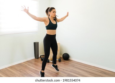 Healthy woman with black sporty clothing working out with jumping jacks and sweating during her daily cardio exercises at home - Shutterstock ID 1981554074