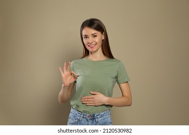 Healthy woman holding hand on belly and showing OK gesture against beige background