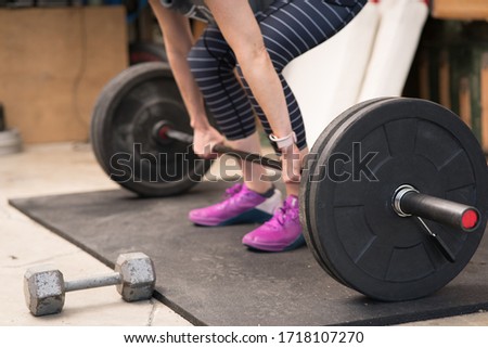 Healthy woman performing a weight lifting deadlift movement in a home gym (garage)