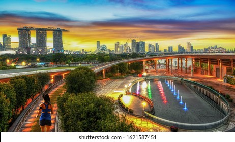 Healthy Woman Running Exercise In Marina Bay Barrage Park At Sunset, Singapore City, Singapore.