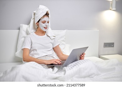 Healthy Woman Sitting On Bed With Face Beauty Mask Using Laptop And Working Online. Cozy Time At Home. Self Time And Home Spa Concept. Coronavirus Outbreak And Self-quarantining Concept