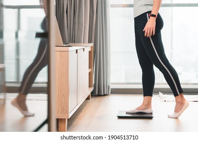 A healthy woman standing on a scale to measuring her weight in the living room after home workout in the morning. Body mass index - BMI, Hormones, Weight Loss, ideal healthy weight, Metabolism, Diet.
