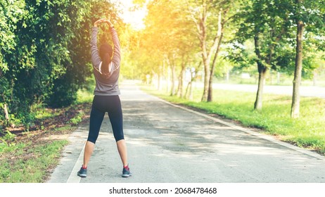 Healthy woman warming up before jogging run and relax stretching her arms and looking away in the road outdoor. Asian runner people workout fitness nature park background