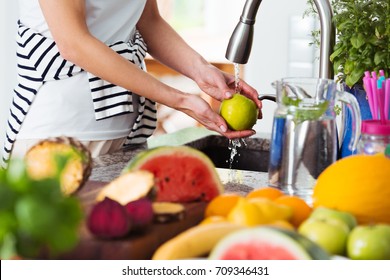 Healthy woman washing an apple above kitchen sink while preparing fresh breakfast with fruit
