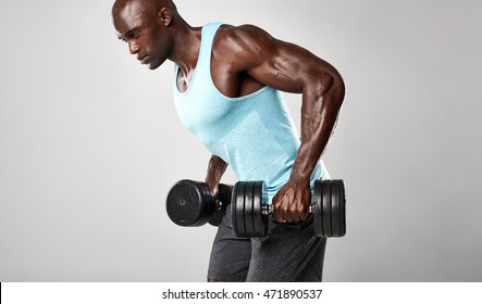 Healthy young african man exercising with dumbbells. Muscular black male model lifting heavy dumbbells against grey background.