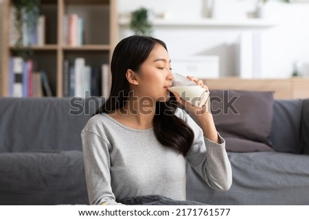 Healthy Young Asian woman Drinking milk with calcium for strong bone at home. Smiling indian woman holding soy milk on glass enjoy with nutrition wellness life.Wellness with natural milk fresh Concept