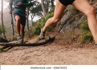 Healthy young couple running on mountain trail in morning. Young man and woman jogging on country path, focus on legs.