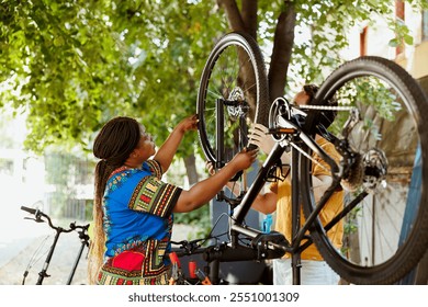 Healthy young interracial couple fixing bicycle with professional equipments.Young energetic caucasian man and african american woman doing maintenance on bike gear as outdoor hobby. - Powered by Shutterstock