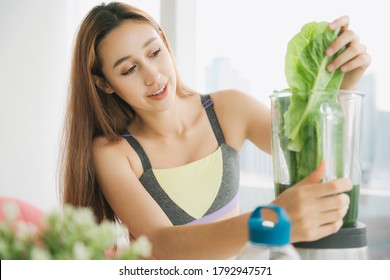 Healthy young woman in sport bra at kitchen making fresh vegetable juice in juicer blending machine, preparing nutritious vitamin packed drink.Healthy woman blending green vegetable in mixing machine. - Powered by Shutterstock