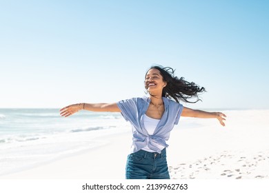 Healthy young woman standing on the beach with hands outstretched. Happy smiling latin woman with open arms feeling the breeze on seaside. Natural beauty woman with outstretched arms up dancing at sea