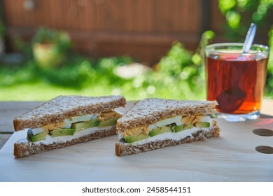 Healty and balanced breakfast served in the garden during sunny summer morning. Sandwich made from wholegrain bread, hard boiled egg, slices of fresh avocado and spreadable fresh cheese with black tea - Powered by Shutterstock