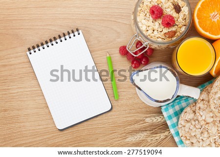 Healty breakfast with muesli, berries and orange juice. View from above on wooden table with notepad for copy space
