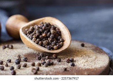 Heap of black pepper, peppercorns in spoon with milled powder on rustic background, dried spice peppercorn concept