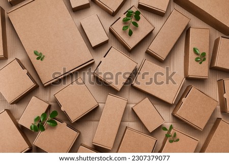 Heap of cardboard boxes from natural recyclable materials with green leaves sprout top view. Responsible consumption, eco friendly packaging, zero waste concept.