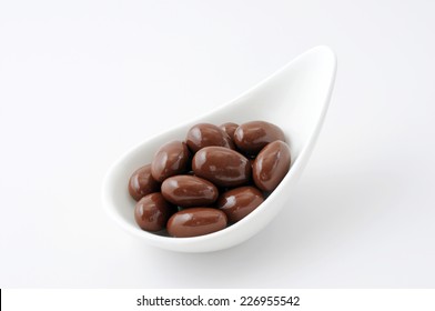 A Heap Of Chocolate Covered Almonds On A Plate On White Background