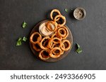 Heap of deep fried onion rings on wooden serving dish on brown background. Top view, flat lay
