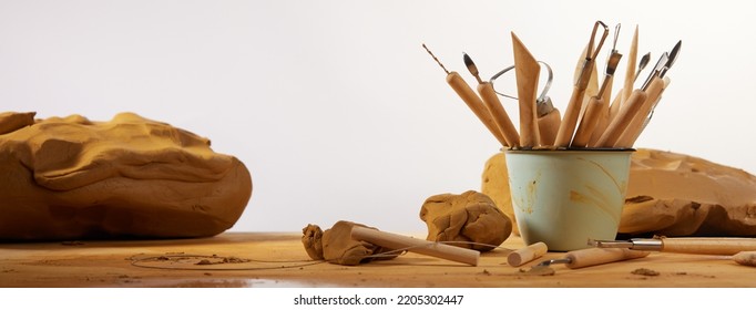 Heap of different tools for modeling pottery placed on table with clay against white background in light workshop