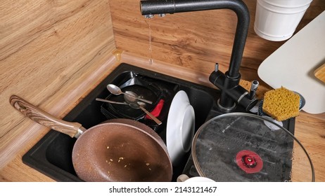 Heap Of Dirty Dishes After Cooking Dinner Lies In Kitchen. Broken Faucet Leaks Dropping Water On Utensils In Sink At Wooden Countertop Close View