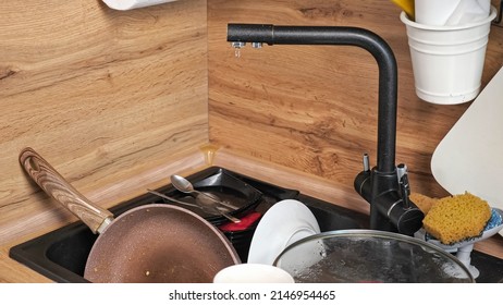 Heap Of Dirty Dishes After Cooking Dinner Lies In Kitchen. Broken Faucet Leaks Dropping Water On Utensils In Sink At Wooden Countertop Close-up