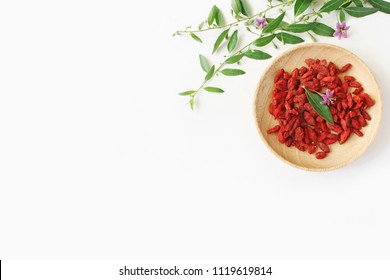 Heap Of Dried Goji Berries Fruit, Lycium Barbarum In Wooden Bowl On White Table. Blossoming Wolfberry Herbal Plant Branch. Healthy Superfood. Flatlay, Top View.  