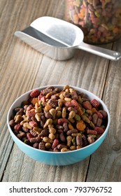 Heap Of Dry Pet Food In Blue Plastic Bowl On Rustic Wooden Floor With Metal Scoop And Storage Jar