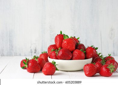 Heap of fresh strawberries in ceramic bowl on rustic white wooden background. 