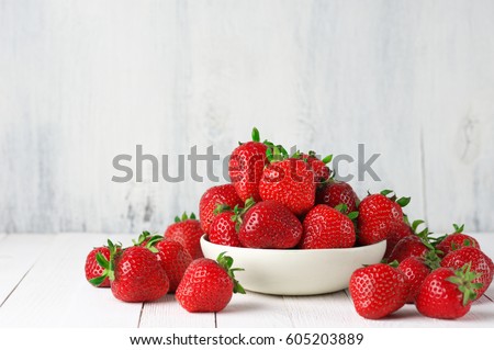 Heap of fresh strawberries in ceramic bowl on rustic white wooden background. 